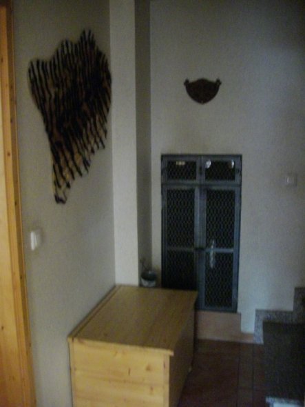 Blick zur Treppe. Eine Holztruhe, Fellimitat an der Wand, Gitter vom "Schürloch" des Kachelofens.